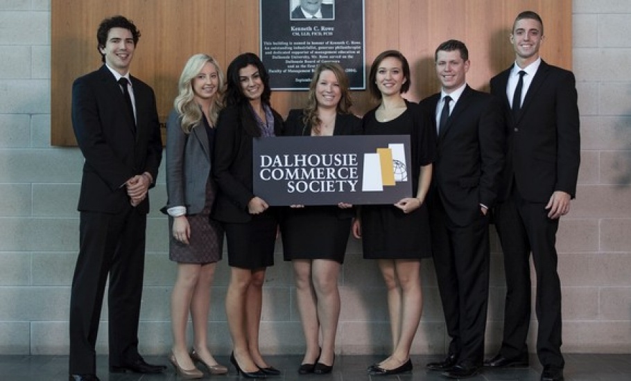 Seven people stand in the Rowe Management Building atrium holding a sign: DALHOUSIE COMMERCE SOCIETY.