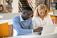Two people working on a laptop in a library.